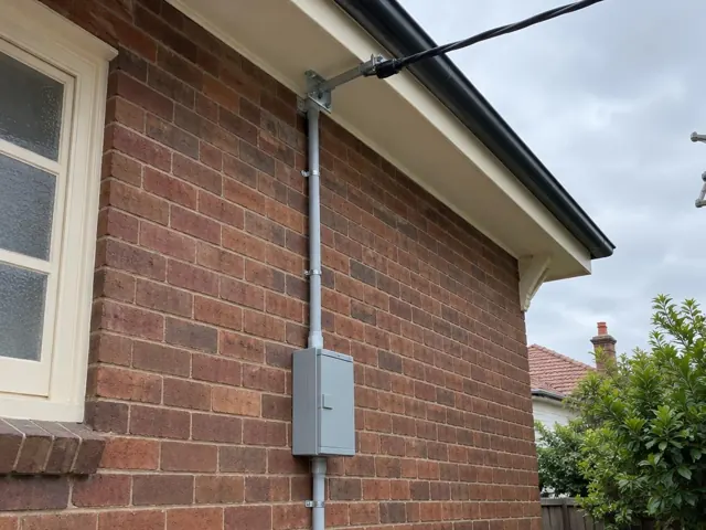 Overhead service cable and point-of-attachment bracket on a brick house exterior in Lane Cove